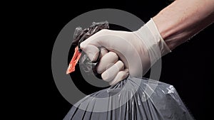 Hand in a protective glove gives a full garbage bag on a black background.