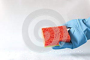 Hand in protective glove holding red sponge against brigth wet surface and water drops on it.Concept of house cleaning and dish wa