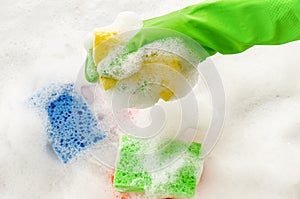 Hand in protective glove holding a soapy sponge on foam background.