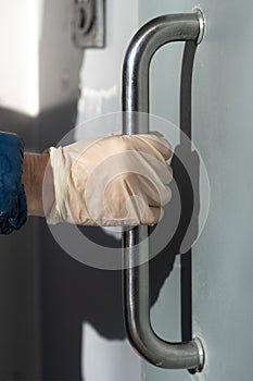 Hand in a protective glove to prevent coronavirus infection opens the door by the metal handle