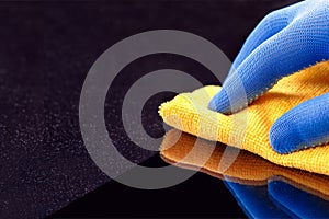 Hand in protective glove wiping dust layers on the furniture  with yellow dry rag. General or regular cleanup.