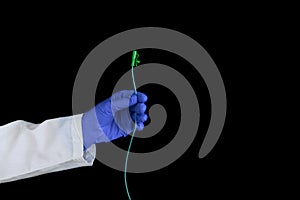 A hand in protective surgical blue gloves holds urological catheter on a black background