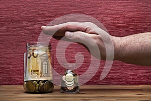 Hand protects euro coins and bill on the burgundy red background in a money box