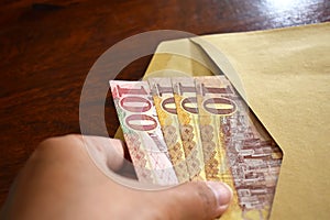 Hand pulling 10 Riyal and 100 Riyal Saudi banknotes from an envelope.