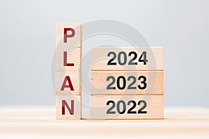 hand pulling 2024 block over 2023 and 2022 wooden building on table background. Business planning, Risk Management, Resolution,