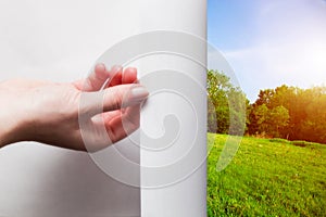 Hand pulling edge of a paper to uncover green landscape