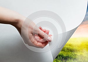 Hand pulling a paper corner to uncover, reveal green landscape photo