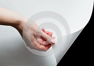 Hand pulling a paper corner to uncover, reveal something