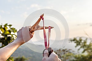 Hand pulling slingshot to shoot tree seed into forest.