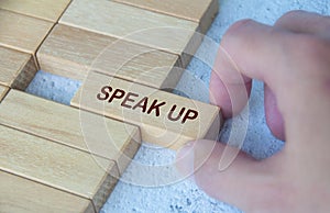 Hand pulling wooden block with text SPEAK UP. Courage concept
