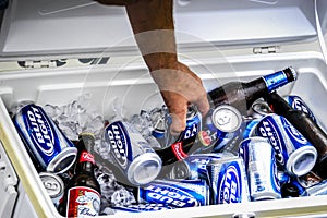 A hand pulls a beer from a cooler box