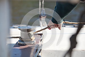 Hand pulls the rope around winch of sailboat closeup