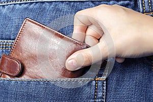 A hand pulls a wallet out of the back pocket of his jeans.The concept of pickpocketing or theft in the family from parents.Close