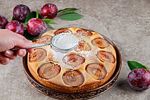 Hand puring powdered sugar on plum pie