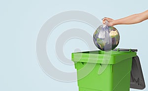 a hand pushing a ball into a green container with trash