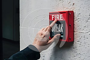 Hand pushing BREAK GLASS fire alarm box on white wall, emphasizing emergency readiness photo