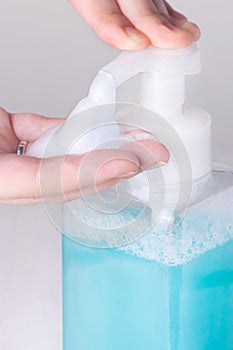 Hand pushing foam bubbles from plastic transparent bottle dispenser  with blue liquid soap macro