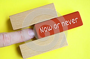 Hand pushing red wooden block with now or never text