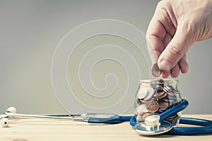 Hand put coin in a jar wrapped in a stethoscope