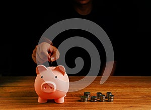 Hand put coin into piggy bank, saving cash coin concept investment. Management growth funding budget for wealth. Wooden background