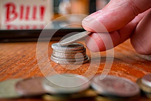 Hand put coins to stack of coins. In background a blurred inscription BILL! and a pile of coins in the foreground