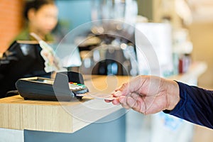 Hand put credit card In slot of credit card reader with blurry cashier at counter service, credit card payment, buy and sell