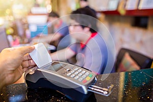 Hand put credit card In slot of credit card reader with blurry cashier and customer at counter service