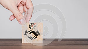 Hand put a handshake icon on wooden cubes block. Business partner or mergers and acquisitions concept.