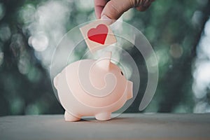 Hand put heart in pink piggy bank. Concept of Insurance for your health