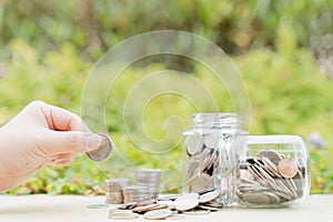 Hand put money coin into jar on blurred green natural background. Saving money and investment concept