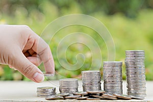 Hand put money coin on stack coins on blurred green natural background. Property investment and house mortgage financial concept