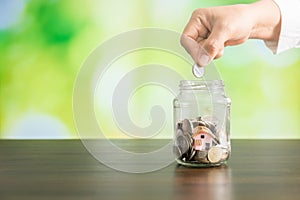 hand put money coins in glass of jar and green bokeh