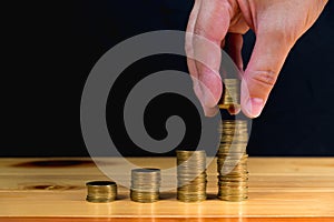 Hand put money gold coins to stack of coins on wooden table with