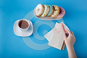 Hand put pen on painting heart with tea and donuts