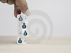 Hand put a white cube block with the dollar money bag icon symbol on the top of stack on white background with copy space.