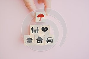 hand put wooden cube block screen  umbrella icon on top of  family, heart, graduationhat, house and car symbol for