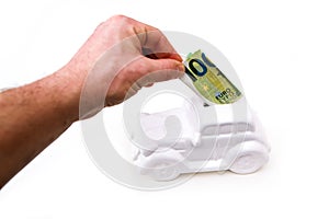 The hand is puting a banknote into the ceramic car shaped money box