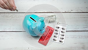 Hand puts a coin in the piggy Bank. Pills, medications are on the table. The concept of savings, pharmacy business, paid