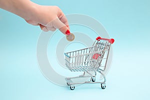 The hand puts a coin in the shopping cart. The concept of saving in stores and everyday grocery shopping