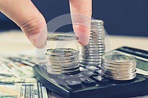 A hand puts coins over a stack of coins against the background of a calculator. Depicts financial investments. Stock market or bus