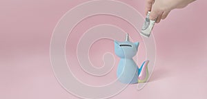 Hand puts a dollar in the kitty`s piggy Bank corn blue with a colorful rainbow tail and unicorn horn on a pink