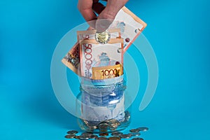 The hand puts a tenge coin in a glass jar with money. Kazakhstan. KZ. KZT. Banknote, paper currency, coins, Bank. Salary, credit,