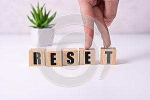 The hand puts a wooden cube with the letter R from the word Reset. The word is written on wooden cubes standing on the yellow