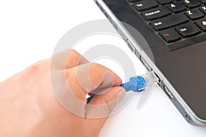 Hand putting a blue RJ45 network connecting cable to a laptop