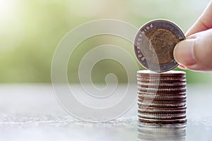 Hand putting a coin, 10 Baht Thai currency money on the stack of