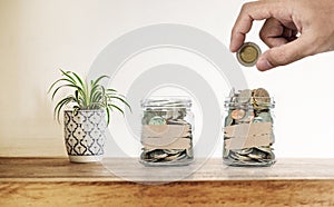Hand putting coin in glass bottles, with decoration plant on wooden desk, Saving money , investment and economize concepts photo