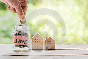 Hand putting coin in glass jar of coin for saving money for buying house.