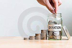 Hand putting coin in jar word donation with money stack, Concept