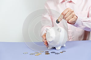 Hand putting coin into piggy bank closeup. Selective focus