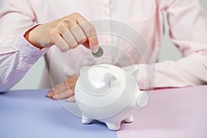 Hand putting coin into piggy bank closeup. Selective focus